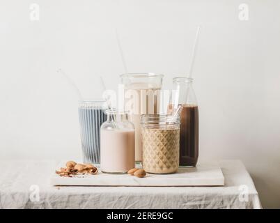 Mandelmilchfreie Milch mit blauen Matcha, Beeren, Kaffee, Zimt, Kakao in Flaschen und Gläsern und Nüssen Zutaten an Bord über Tischdecke, weiß Stockfoto