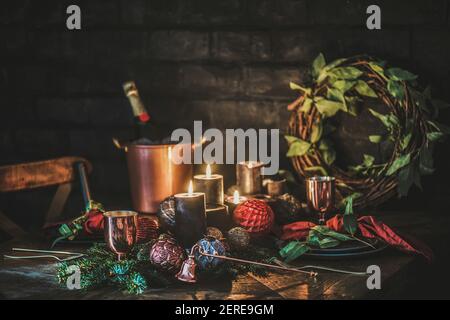 Weihnachtsfeiertag festliche Tischkulisse. Geschirr, Besteck, Flasche Champagner in Eiskübel, Weihnachtskranz auf Vintage-Holztisch mit dekoriert Stockfoto