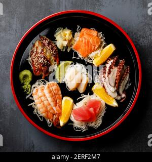 Sashimi Sushi-Set mit Daikon und Zitrone auf traditionellem Japan Schwarze Sushioke runde Platte auf dunklem Hintergrund Stockfoto