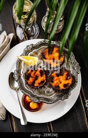 Frisch geöffnete Seeigel auf Eis in silberner Schüssel mit Wachtelei und Sojasauce und Champagner auf schwarzem Holz Tabelle Stockfoto