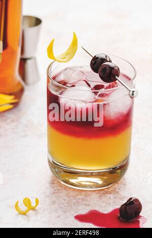 New York Whiskey Sour im Glas mit Eiswürfeln, Kirschen darauf mit Sirup und Zitronenschale garniert. Stockfoto