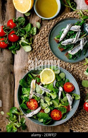 Grüner Feldsalat mit eingelegten Sardellen oder Sardinenfilet und Kirschtomaten, serviert in blauer Schüssel mit Zitrone und Olivenöl auf Strohserviette über ol Stockfoto