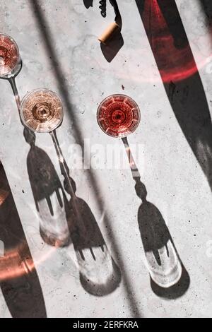 Drei Schattierungen von Rose´ Wein in Gläsern, die harte Schatten werfen, umgeben von bunten Schatten aus den Weinflaschen. Stockfoto