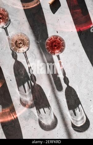 Drei Schattierungen von Rose´ Wein in Gläsern, die harte Schatten werfen, umgeben von bunten Schatten aus den Weinflaschen. Stockfoto