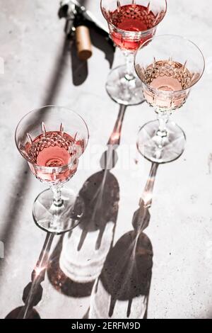 Drei Rosétöne´ Wein in Gläsern, die harte Schatten neben einem Korkenzieher werfen. Stockfoto