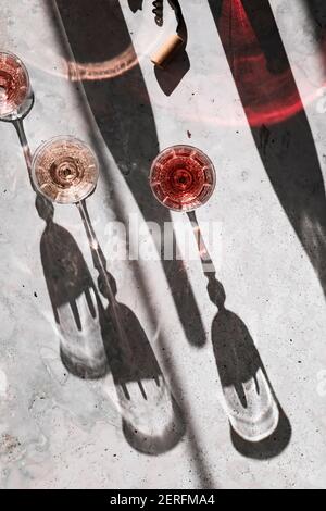 Drei Schattierungen von Rose´ Wein in Gläsern, die harte Schatten werfen, umgeben von bunten Schatten aus den Weinflaschen. Stockfoto