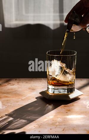 Whiskey wird in hartem Licht in ein Steinglas gegossen. Stockfoto
