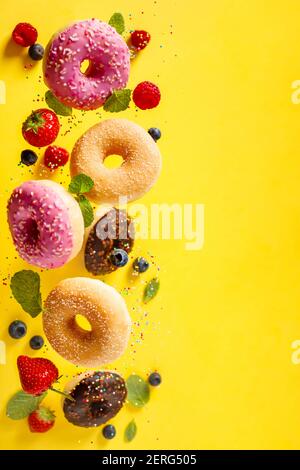 Verschiedene dekoriert Donuts mit Streuseln und Beeren in der Bewegung des Fallens auf yelloy Hintergrund. Süß und bunt Donuts fallen oder Fliegen in moti Stockfoto