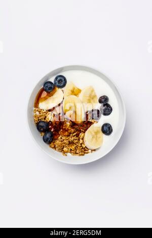 Gesunde vegetarische Frühstück - Hafer Müsli mit frischen Blaubeeren, Bananen, Soja Joghurt und Ahornsirup auf weißem Hintergrund, Flach, Ansicht von oben Stockfoto