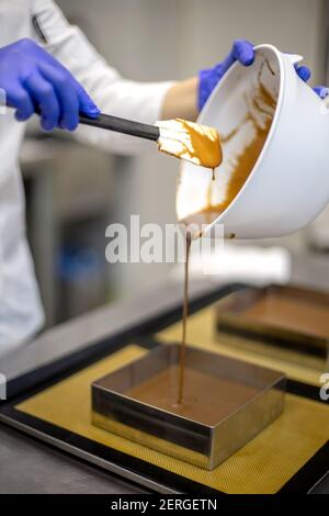 Lächelnde weibliche Konditorin Gießen Schokolade Gomage auf Kekskuchen Montage Mousse Dessert Stockfoto