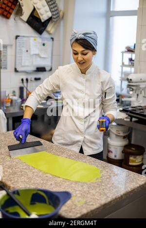 Frau Konditor in Uniform Gießen flüssige Matcha Tee Schokolade auf Tisch aus Schüssel bei der Küche Stockfoto
