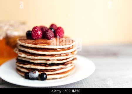 Saftige Pfannkuchen mit Beeren und Honig auf einem weißen Teller, Löffel, Glas, Holztisch. Hochwertige Fotos Stockfoto