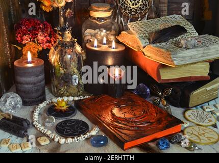 Stillleben mit Grimoire Buch der Zaubersprüche, brennende Kerzen, Runen und rituelle Objekte auf Hexentisch. Esoterischer, gotischer und okkulter Hintergrund, Halloween m Stockfoto