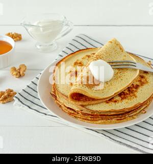 Pfannkuchen mit Honigsirup und saurer Sahne auf einem weißen Teller serviert. Traditionelle Crepes für Pancake Week oder Shrovetide Stockfoto