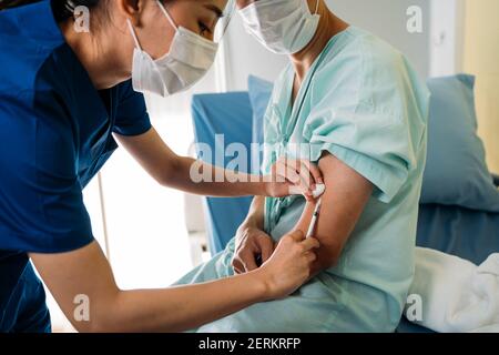 Nahaufnahme einer jungen Ärztin in Uniform mit Gesichtsmaske Während der Impfung Injektion an jungen männlichen Patienten trägt ein Maske zur Sicherheit gegen covid-19 Pandemie Stockfoto