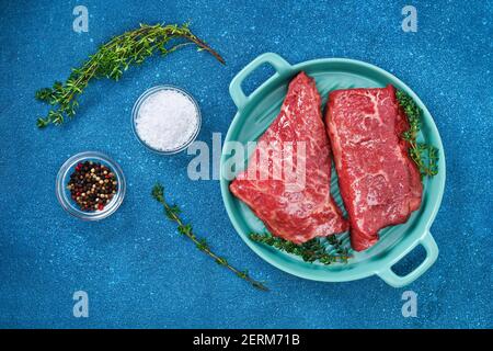 Rohes Steak auf einem Schneidebrett mit Rosmarin und Gewürzen, blauer Hintergrund, Draufsicht. Frisch gegrilltes Fleisch. Gegrilltes Rindersteak. Stockfoto