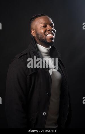 Schöner schwarzer Mann lächelt. Mittlerer Schuss. Schwarzer Hintergrund Stockfoto