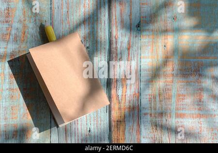 Notizblock mit gelbem Stift auf rustikalem Holztisch mit Schatten von Palmblättern. Speicherplatz kopieren. Stockfoto