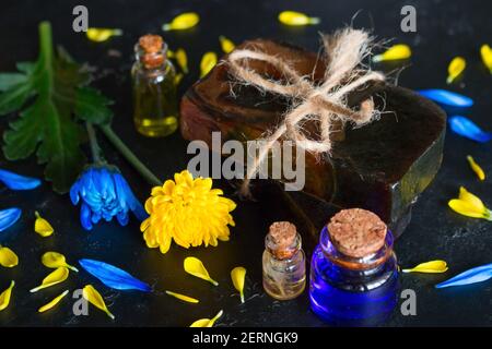 Handgemachte Seife aus Blumen und Flaschen mit Kosmetiköl auf Schwarzer Hintergrund Stockfoto