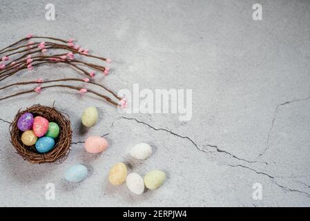 Bunte Ostereier im Vogelnest mit dekorativen Weidenzweigen Auf grauem Zementhintergrund Stockfoto
