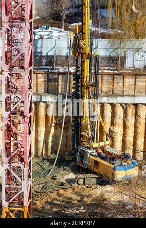 Ein Schwerbagger, zusammen mit einem Bohrgerät, arbeitet auf einer Baustelle, um das Fundament für ein zukünftiges Hochhaus zu stärken. Vertikales Bild. Stockfoto