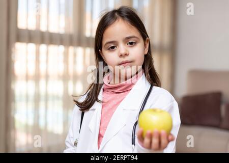 Porträt eines kleinen Kindes, das als Krankenschwester gekleidet ist und einen Apfel in der Hand zeigt. Konzept von Wohlbefinden und gesundes Leben. Leerzeichen für Text. Stockfoto