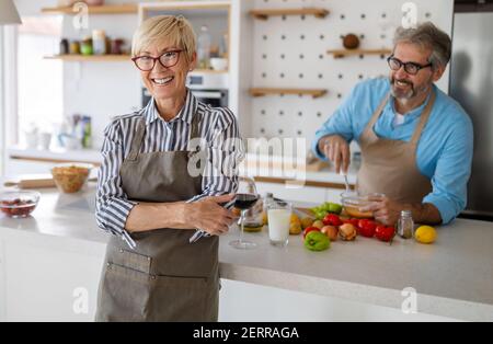 Ältere Paare, die Spaß haben, kochen und Wein trinken in der heimischen Küche Stockfoto