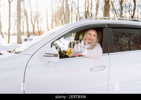 Junge blonde Frau sitzt in ihrem neuen weißen Auto und lächelt glücklich. Versicherung, Sicherheit. Stockfoto