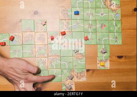 Russland, Dezember 2020: Hand des Mannes, der das Brettspiel carcassonne auf dem Tisch spielt, in der Nacht, Draufsicht Stockfoto