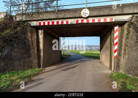 Eisenbahntunnel, der zur Straße zum Ackerland führt, Dorf in der Ferne und Warnschilder. Stockfoto