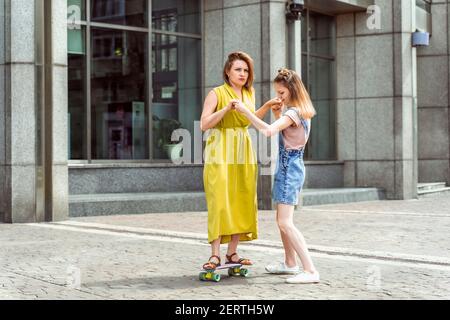 Kaukasische Teenager-Mädchen lehrt ihre Mutter, wie man Skate. Aktiver Familienleben Stockfoto