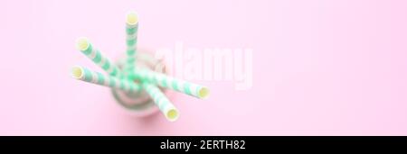 Verschwommener Papierstapel gestreift weiß und grün Trinkhalme für Party in Klarglas kleine Flasche auf rosa Hintergrund. Platz für Text. Banner Stockfoto