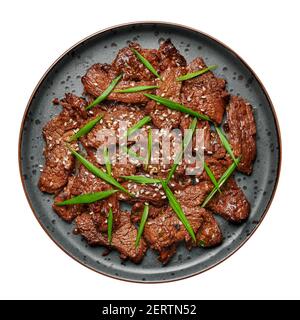 Rindfleisch Bulgogi auf schwarzem Teller isoliert auf weiß. Koreanische Küche Fleischgericht mit Sauce und Kiwi. Traditionelles asiatisches Essen. Draufsicht Stockfoto