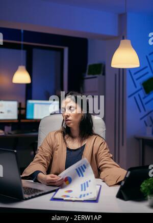 Unternehmer durch Dokumente suchen, um eine Frist am Abend zu beenden. Geschäftsfrau arbeitet Überstunden im Büro, um eine Unternehmensarbeit mit Tablet-pc zu beenden. Stockfoto