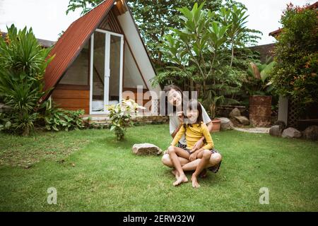 Nette kleine asiatische Mädchen Unterstützung ihrer Mutter spielen und haben Spaß in einem Hinterhof. Stockfoto