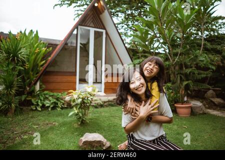 Nette kleine asiatische Mädchen Unterstützung ihrer Mutter spielen und haben Spaß in einem Hinterhof. Stockfoto