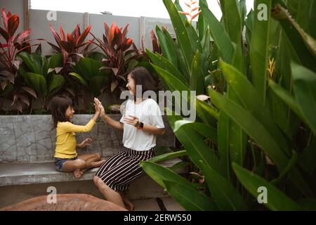 Nette kleine asiatische Mädchen Unterstützung ihrer Mutter spielen und haben Spaß in einem Hinterhof. Stockfoto