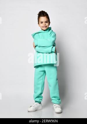 Full-Growth Porträt von frolic lächelnden Jungen Kerl mit stilvollen Haarschnitt in Pastell modern grün, mintfarben Hoodie, Sweatshirt stehend umarmt sich und Stockfoto