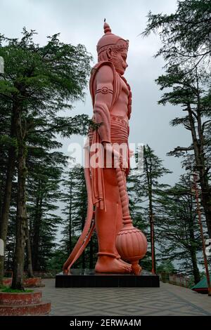 Riesige öffentliche Statue des hinduistischen Gottes, Lord Hanuman, flankiert von hohen Kiefern mit Blick auf Himalaya in Shimla, Himachal Pradesh, Indien. Stockfoto