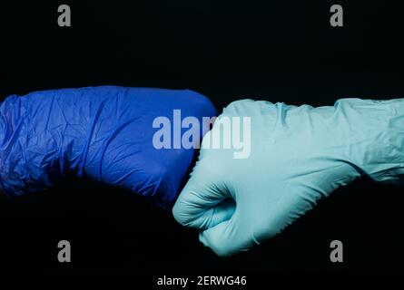 Eine symbolische Form des Grußwortes in der Zeit der Coronavirus-Pandemie. Die zwei Personen stoßen Fäuste zusammen (in Schutzhandschuhen) auf schwarzem Rücken Stockfoto