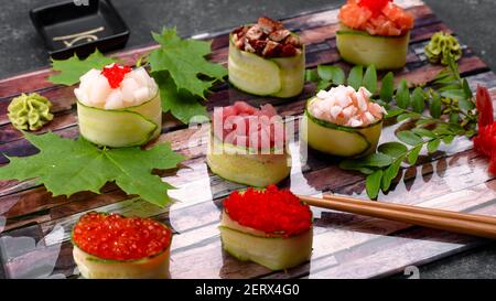 Gunkan Maki in einer Gurke, mit Kaviar, Thunfisch. Jakobsmuschel, Aal, Garnelen, Aal und Lachs, Auf einem Holzbrett, mit Ahorn und Akazienblättern, mit geringer Tiefe Stockfoto