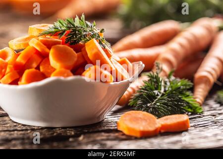 In Scheiben geschnittene Stücke von Karotte in einer Schüssel und eine frische Ein paar Karotten im Hintergrund Stockfoto