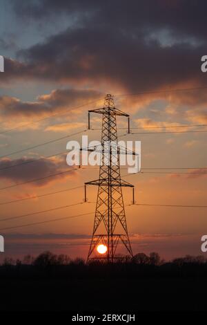 Sonnenuntergang mit einem silhouettierten Hochspannungsmast des National Grid, in Norfolk, England. VEREINIGTES KÖNIGREICH. Stockfoto