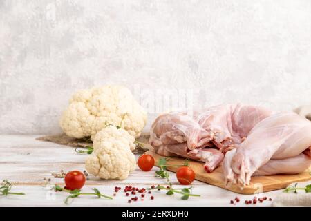 Ganz rohes Kaninchen mit Blumenkohl, Tomaten und Gewürzen auf weißem Holzhintergrund und Leinentextilien. Seitenansicht, Kopierbereich. Stockfoto