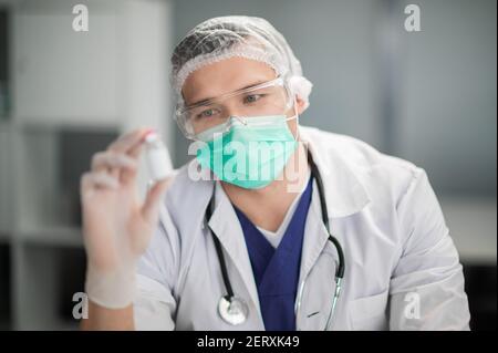 Ein junger, hübscher Labortechniker in einer Schutzbrille untersucht einen neuen Impfstoff Stockfoto