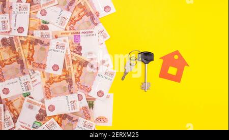 Fünftausend russische Rubel Banknoten auf einem gelben Hintergrund und die Schlüssel für die Wohnung und ein rotes Papierhaus. Das Konzept der Kauf eines Hauses, mortg Stockfoto