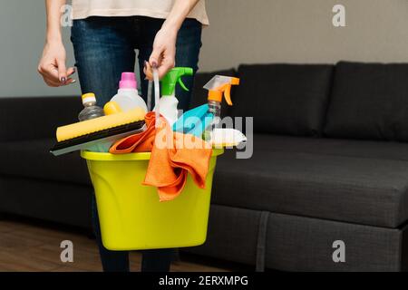 Eine Frau hält Waschmittel in einem Eimer auf dem Hintergrund. Die Frau ist bereit, das Haus zu reinigen. Eine Hausfrau putzt das Haus. Stockfoto