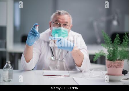 Ein erfahrener Facharzt im Büro empfiehlt ihm Patienten der neueste Coronavirus-Impfstoff in einer Glasampulle Stockfoto