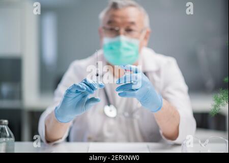 Der Coronavirus-Impfstoff und die Impfspritze liegen in den Händen eines erfahrenen Arztes. Die Arztpraxis in der Klinik medizinischen Stockfoto