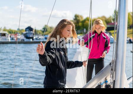 Zwei junge blonde Mädchen an einem sonnigen Sommertag Ein Segelboot bereitet sich auf eine Flussfahrt vor Stockfoto